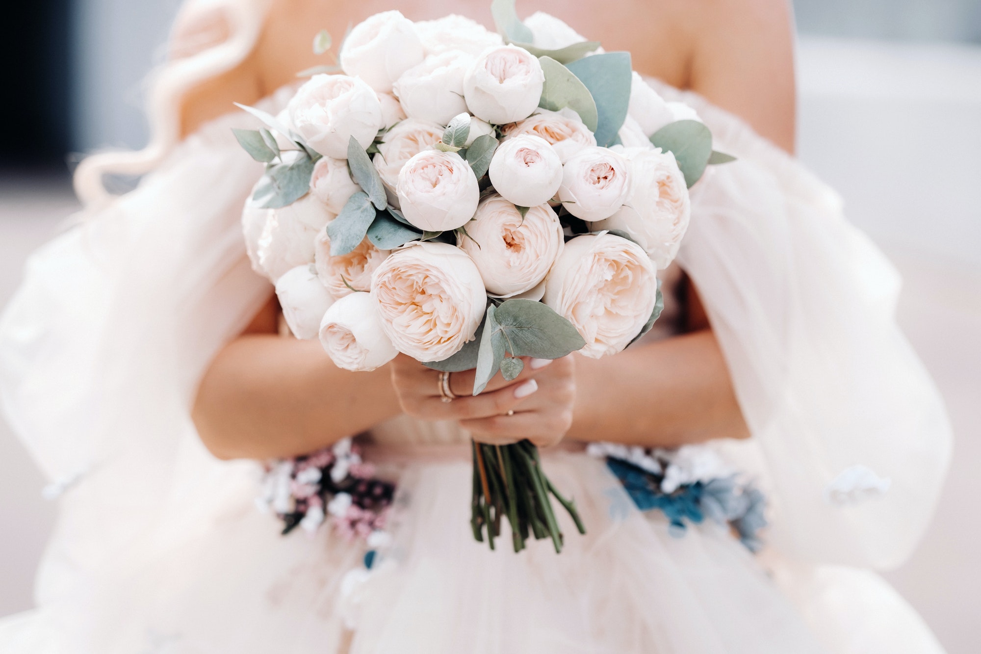 A bride in a wedding dress holds a bouquet of roses in her hands in front of her .close up